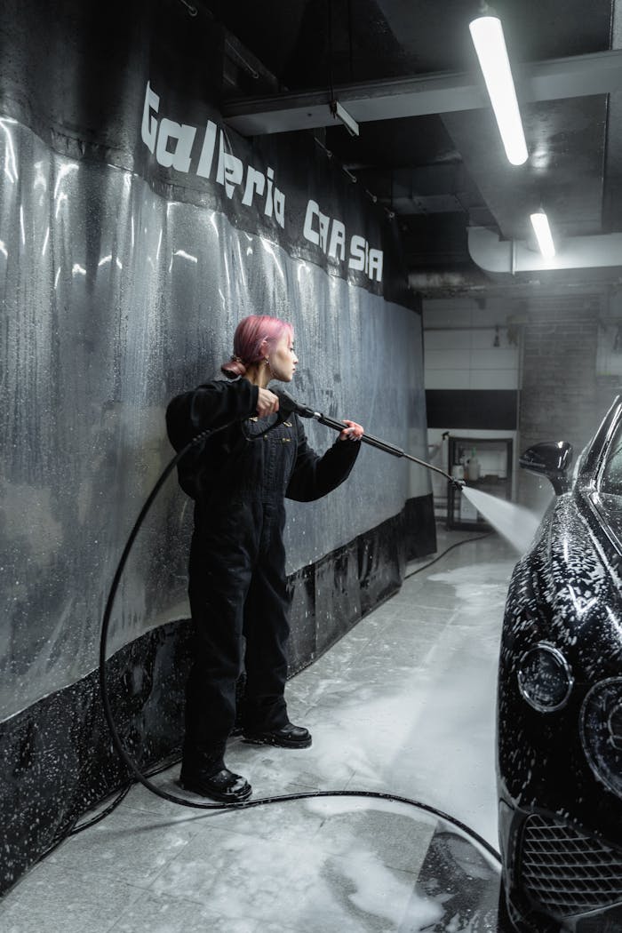 portfolio-06 A young woman in uniform cleans a car with a power spray in an indoor garage setting.